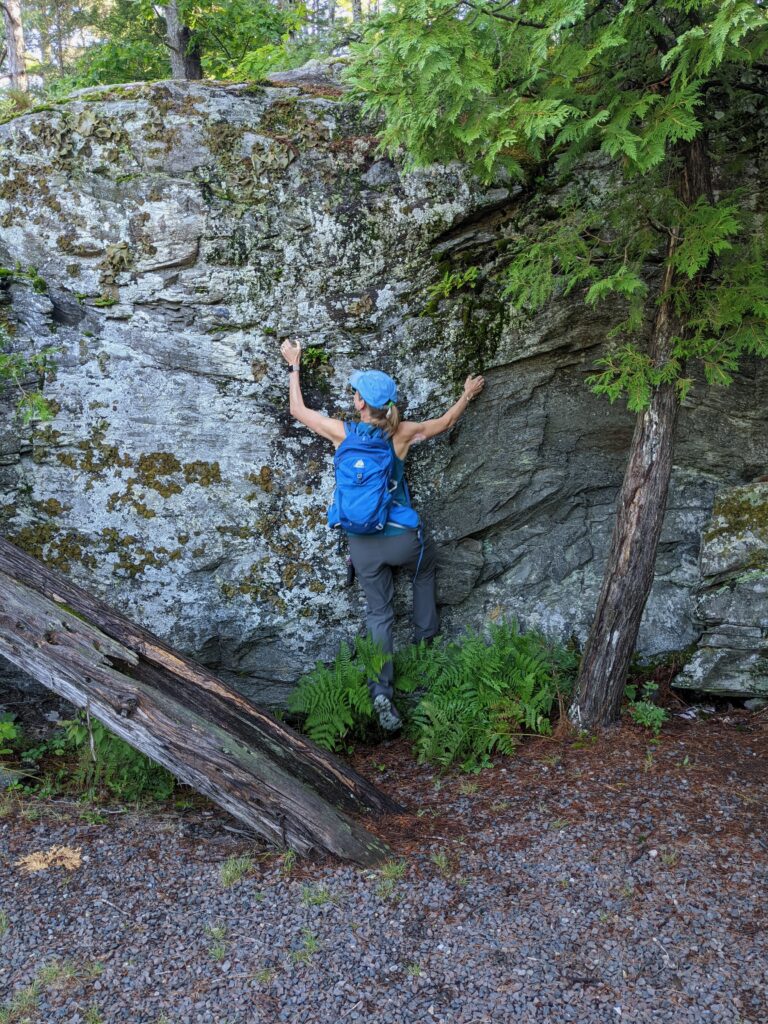 a woman with a blue backpack pretending to climb a rock wall