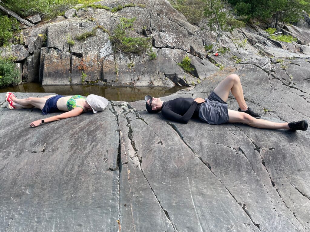 a woman and a man stretched out in swimsuits on a rock in the sun