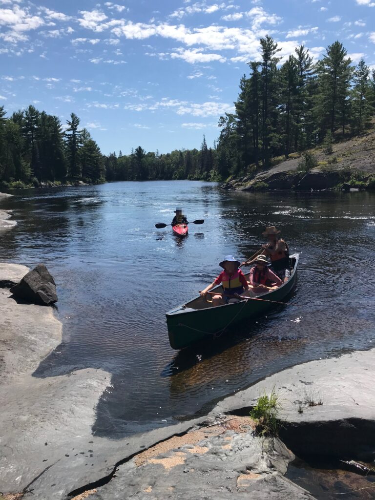 a canoe with 3 people and a kayak with 1 person coming down a river